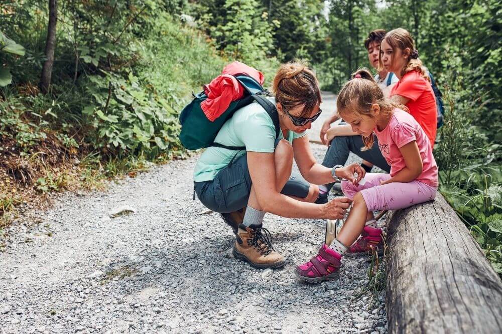 mother bends down to help child with injury while hiking