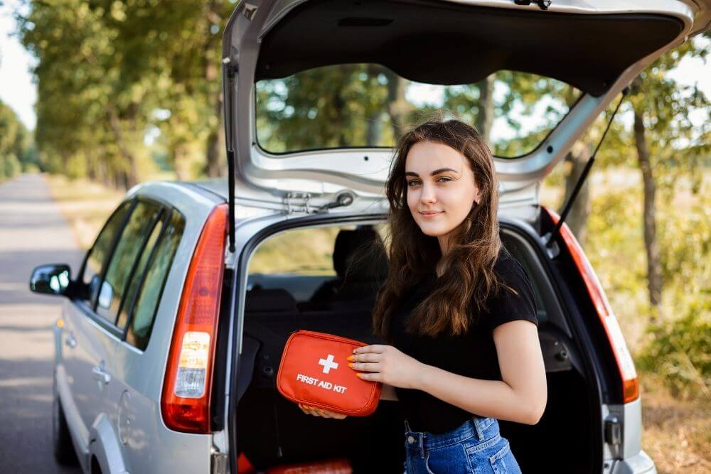 woman standing behind car holding a first aid kit